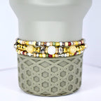 Three beaded bracelets in gold, silver, and cream colors. The bracelets feature a variety of beads, including small gold, silver, and cream-colored beads, and larger, faceted beads. The bracelets are stacked on a gray, geometric-patterned base.