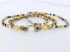 Three beaded bracelets in gold, silver, and neutral tones. The bracelets feature a variety of beads, including faceted metallic beads, small round beads, and larger, smooth beads in yellow and white.