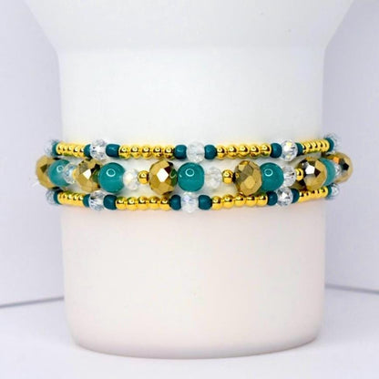 Beaded tumbler bracelet with gold, teal, and clear crystal beads in a layered design. Features faceted metallic gold accents, smooth teal beads, and small gold spacers for a sparkling, elegant look.