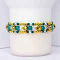 Beaded tumbler bracelet with gold, teal, and clear crystal beads in a layered design. Features faceted metallic gold accents, smooth teal beads, and small gold spacers for a sparkling, elegant look.