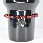 A dark red beaded bracelet with a silver moth pendant. The bracelet features round, glossy red beads interspersed with smaller black beads. The moth pendant is detailed with intricate wing and body patterns, adding a gothic or alternative aesthetic to the jewelry.