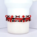 Three beaded bracelets in red, black, and silver. The top bracelet features red and black beads with silver accents and black arrow-shaped beads. The middle bracelet has red and black beads with silver accents. The bottom bracelet is primarily red with black and silver beads.