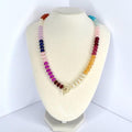 A colorful beaded necklace displayed on a white bust. The necklace features a gradient of colors, including red, orange, yellow, green, blue, and purple beads. It has a gold-colored toggle clasp.