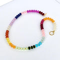 A colorful beaded necklace with a rainbow gradient of colors, including red, orange, yellow, green, blue, purple, and pink. The necklace has a gold clasp and gold accents. The beads are small and round.