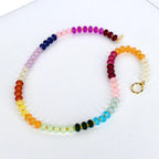 A colorful beaded necklace with a rainbow gradient of colors, including red, orange, yellow, green, blue, purple, and pink. The necklace has a gold clasp and gold accents. The beads are small and round.