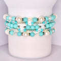 A set of five stacked tumbler bracelets displayed on a white tumbler, featuring a mix of turquoise matte beads, iridescent faceted beads, glossy pearl-like white beads, and shiny silver spacer beads for a vibrant, coastal-inspired design.