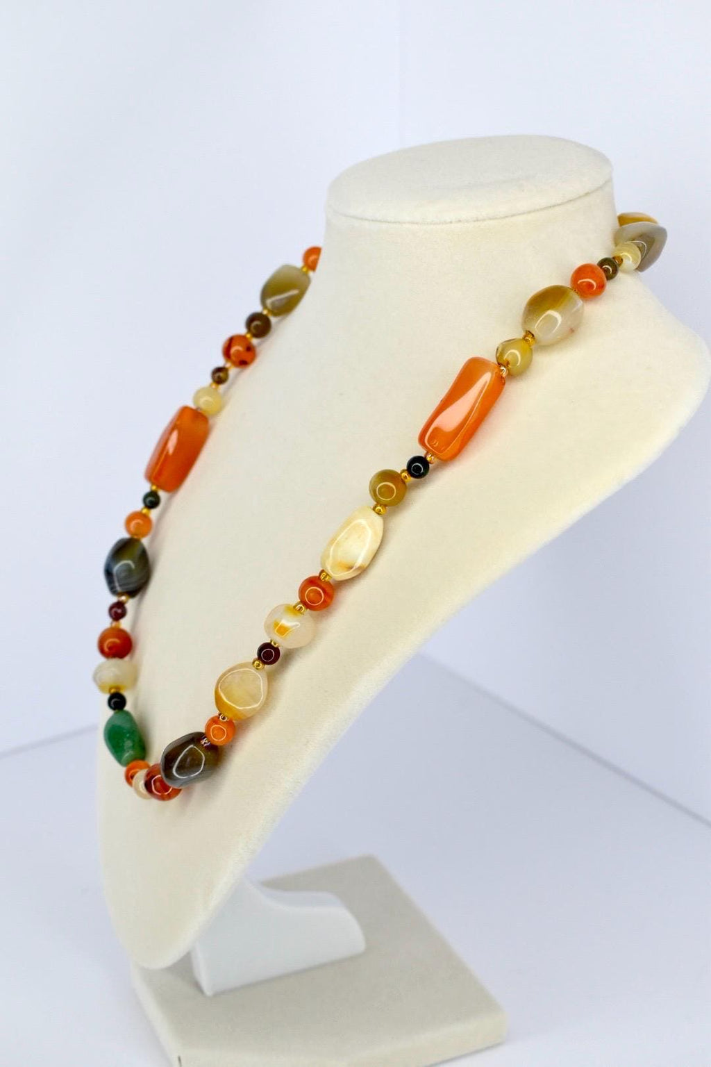 Unique handcrafted necklace with polished semi-precious stone beads in warm earth tones presented on jewelry stand.