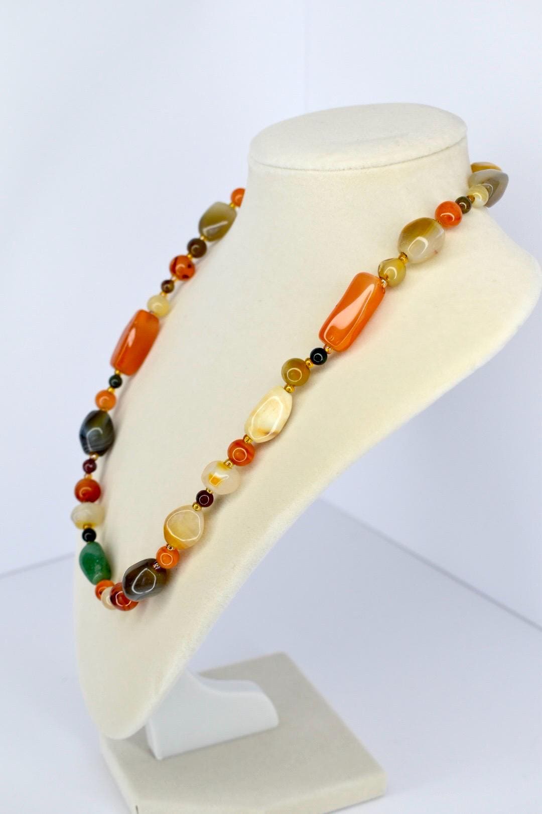 Unique handcrafted necklace with polished semi-precious stone beads in warm earth tones presented on jewelry stand.