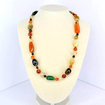 Colorful beaded necklace featuring polished stones in green, orange, amber, and brown tones displayed on a cream jewelry bust.
