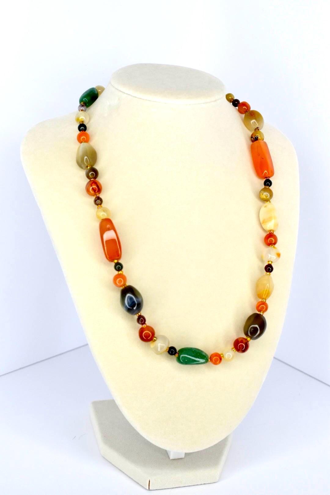 Handmade gemstone necklace with large polished beads in earthy shades of green, orange, yellow, and brown on a display stand.