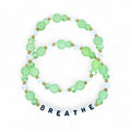 Two beaded bracelets with green and clear beads, and gold accents. The bottom bracelet spells out the word "BREATHE" in white letter beads. The bracelets are on a white background.