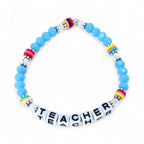 A blue beaded bracelet with the word "TEACHER" spelled out in white letter beads. The bracelet features colorful accent beads with rainbow and striped patterns. The beads are strung on a clear elastic cord.