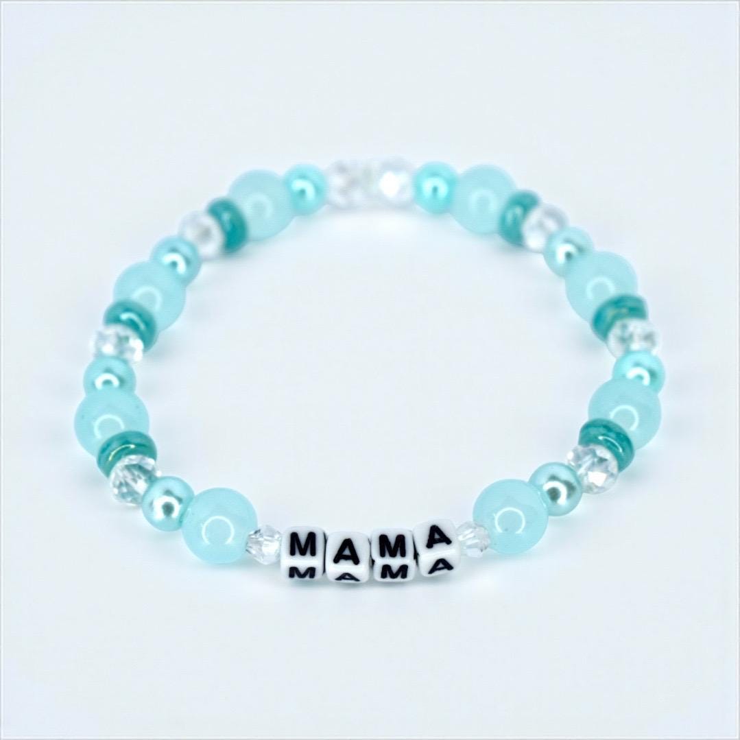 A beaded bracelet featuring light blue and clear beads. The bracelet has the word "MAMA" spelled out in black and white letter beads. The bracelet is a delicate piece of jewelry.