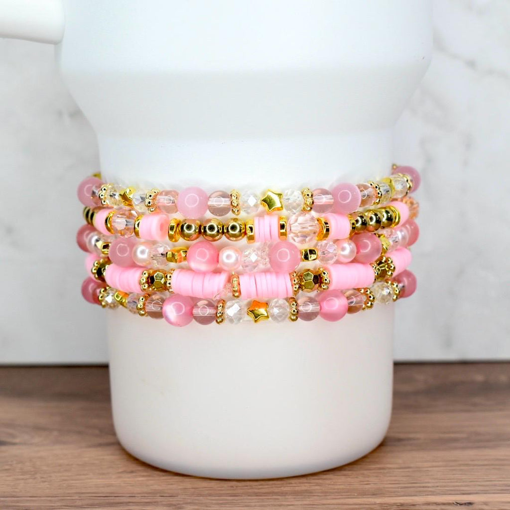 Custom pink and gold beaded bracelet bundle featuring stars, pearls, and word charms, styled on a white tumbler.