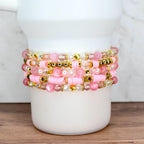 Custom pink and gold beaded bracelet bundle featuring stars, pearls, and word charms, styled on a white tumbler.