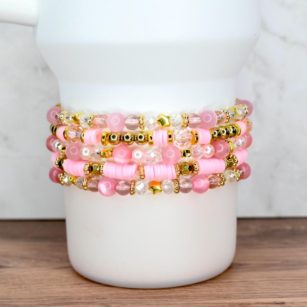 Custom pink and gold beaded bracelet bundle featuring stars, pearls, and word charms, styled on a white tumbler.