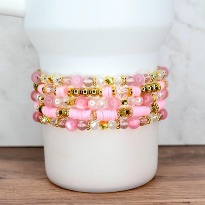 Custom pink and gold beaded bracelet bundle featuring stars, pearls, and word charms, styled on a white tumbler.