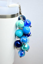 A cluster of blue and iridescent bead charms with a silver-tone clasp. The beads vary in shades of blue, from light turquoise to deep navy, and are attached with small silver accents. The charm is designed to be attached to a tumbler or keychain.
