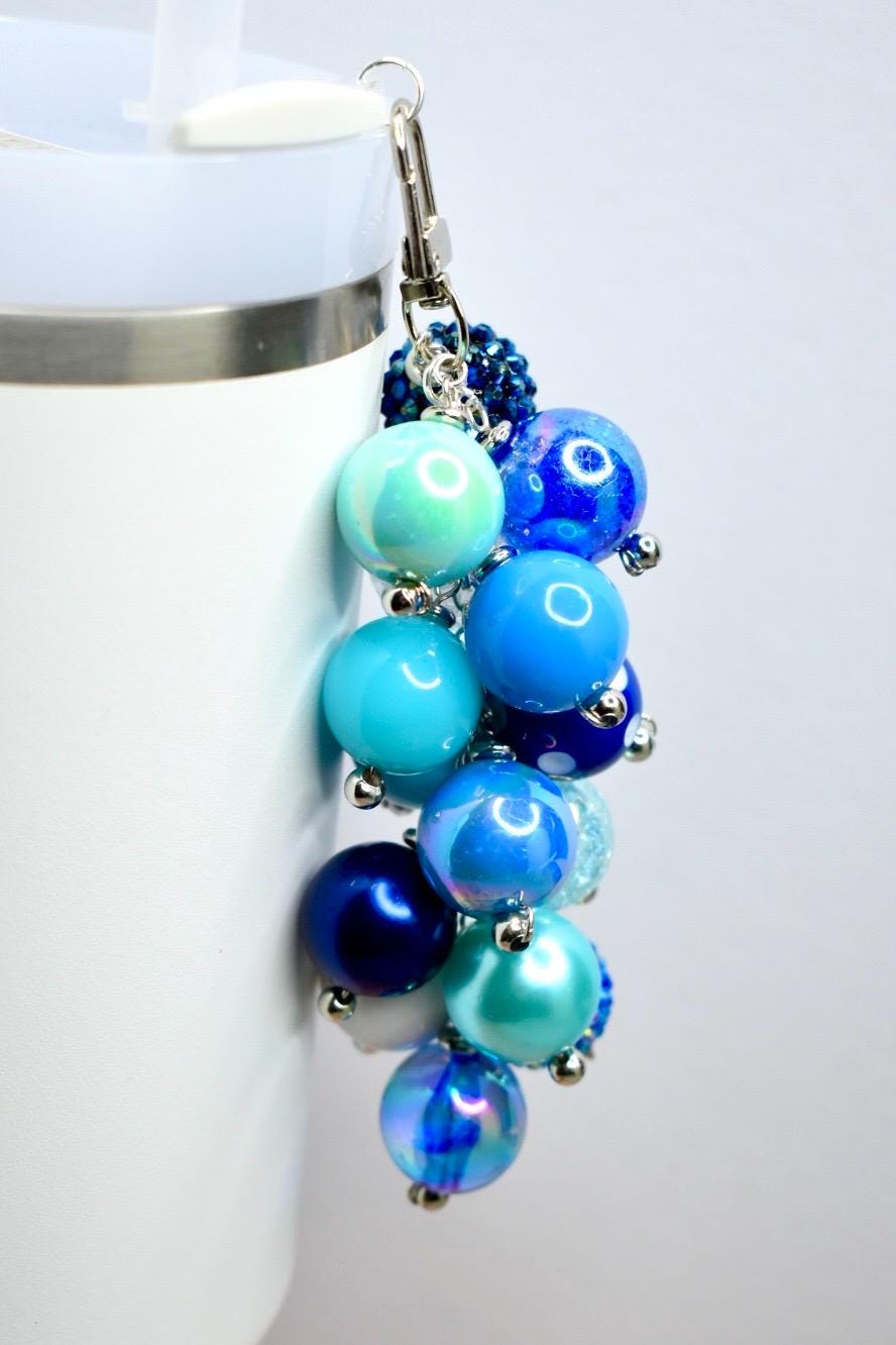 A cluster of blue and iridescent bead charms with a silver-tone clasp. The beads vary in shades of blue, from light turquoise to deep navy, and are attached with small silver accents. The charm is designed to be attached to a tumbler or keychain.