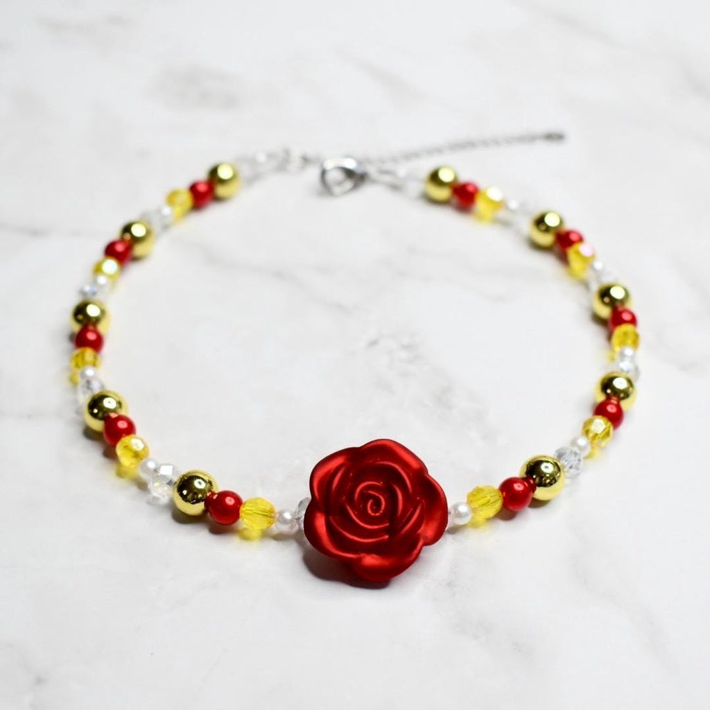 Disney Belle costume jewelry necklace for girls with enchanted red rose charm, gold and red beaded design, adjustable chain, Beauty and the Beast themed kids accessory on marble surface