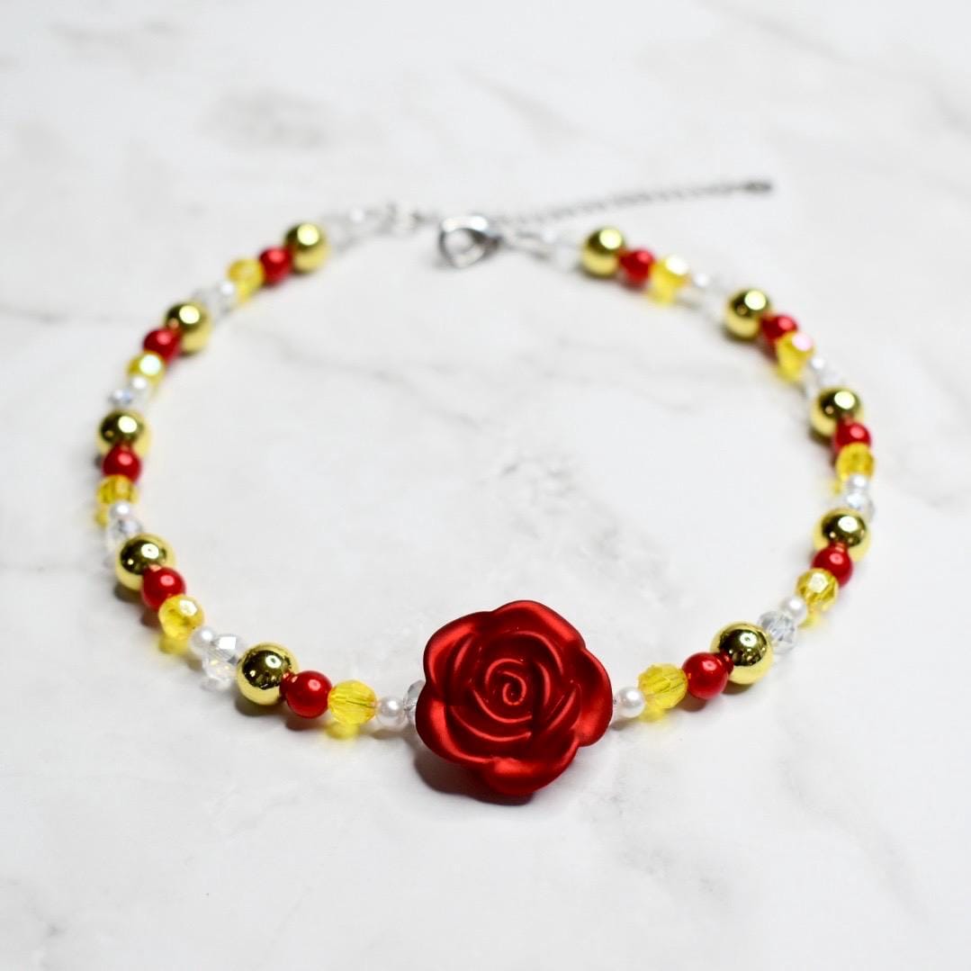 Disney Belle costume jewelry necklace for girls with enchanted red rose charm, gold and red beaded design, adjustable chain, Beauty and the Beast themed kids accessory on marble surface