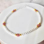 A delicate necklace featuring white faux pearls, interspersed with pink heart-shaped beads and gold-colored accents. The necklace is displayed on a white surface, showcasing its elegant design.