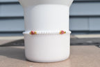 A delicate bracelet featuring small white pearls, accented with pink heart-shaped beads and gold-colored spacers. The bracelet is displayed against a white background, showcasing its elegant design.