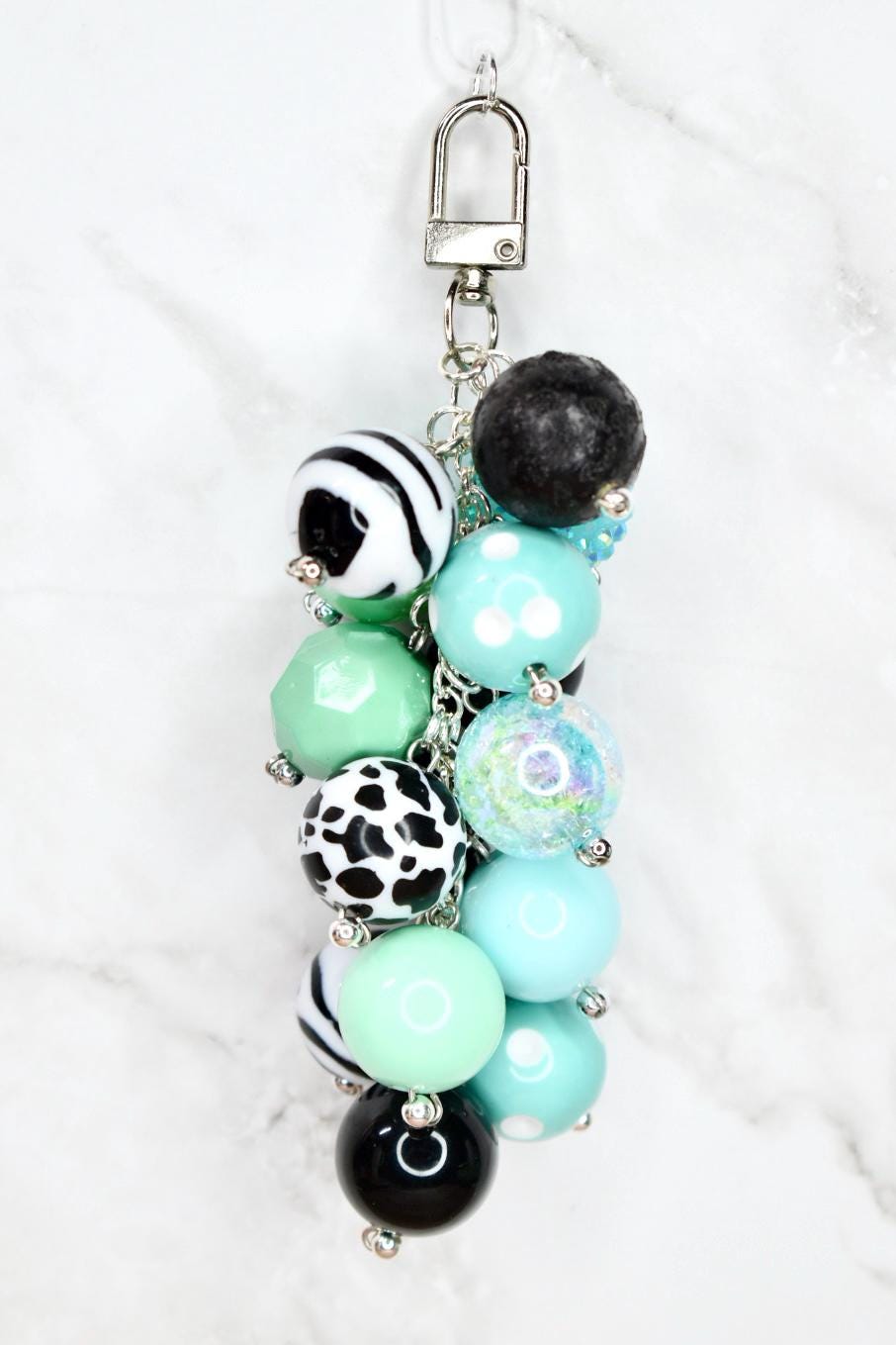 Mint green and black beaded bag charm with cow print pattern beads and lava stone on white marble background