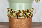 Close-up of a decorative vase with multiple beaded bracelets. The bracelets feature gold, brown, and clear beads. The vase is light green with a glittery copper-colored base.