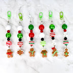 A collection of six Christmas-themed tumbler straw charms. Each charm features a clear plastic clip, a variety of colorful beads in red, green, white, and black, and a gingerbread man or star charm. The charms are designed for attaching to Stanley tumblers.