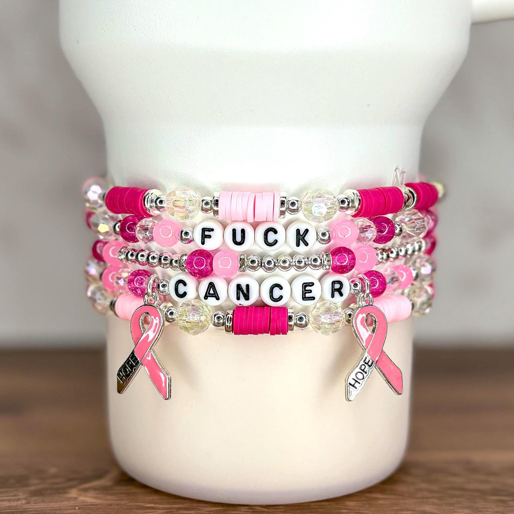 Stack of beaded bracelets in shades of pink, white, and clear. The bracelets have the words "FUCK CANCER" spelled out in white letter beads. Pink ribbon charms with the word "HOPE" hang from the bracelets.