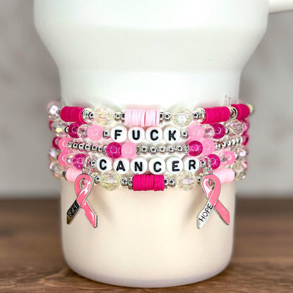 Stack of beaded bracelets in shades of pink, white, and clear. The bracelets have the words "FUCK CANCER" spelled out in white letter beads. Pink ribbon charms with the word "HOPE" hang from the bracelets.