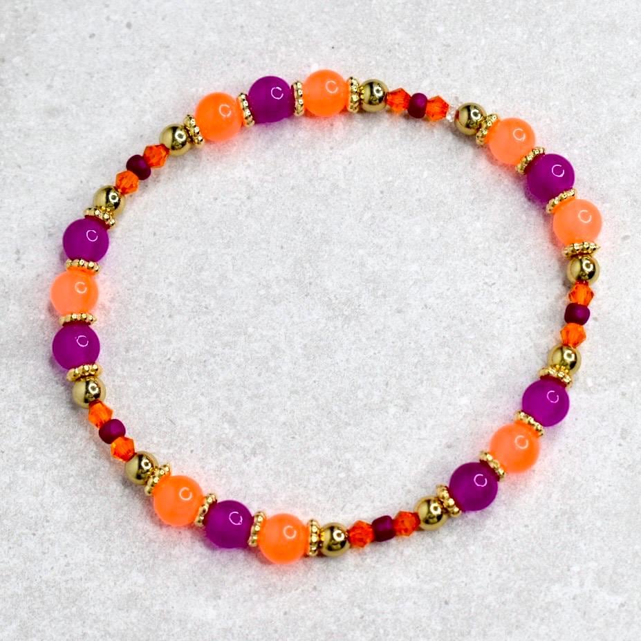 A beaded bracelet featuring alternating orange and purple beads, interspersed with gold-colored beads and smaller orange and red beads. The bracelet is strung on an elastic cord and is designed to be worn around the wrist.