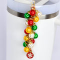 A festive Christmas ornament charm with a cluster of colorful baubles in red, green, yellow, and white. The charm is accented with gold-colored metal and a small red snowflake charm at the bottom. The charm is attached to a white tumbler.