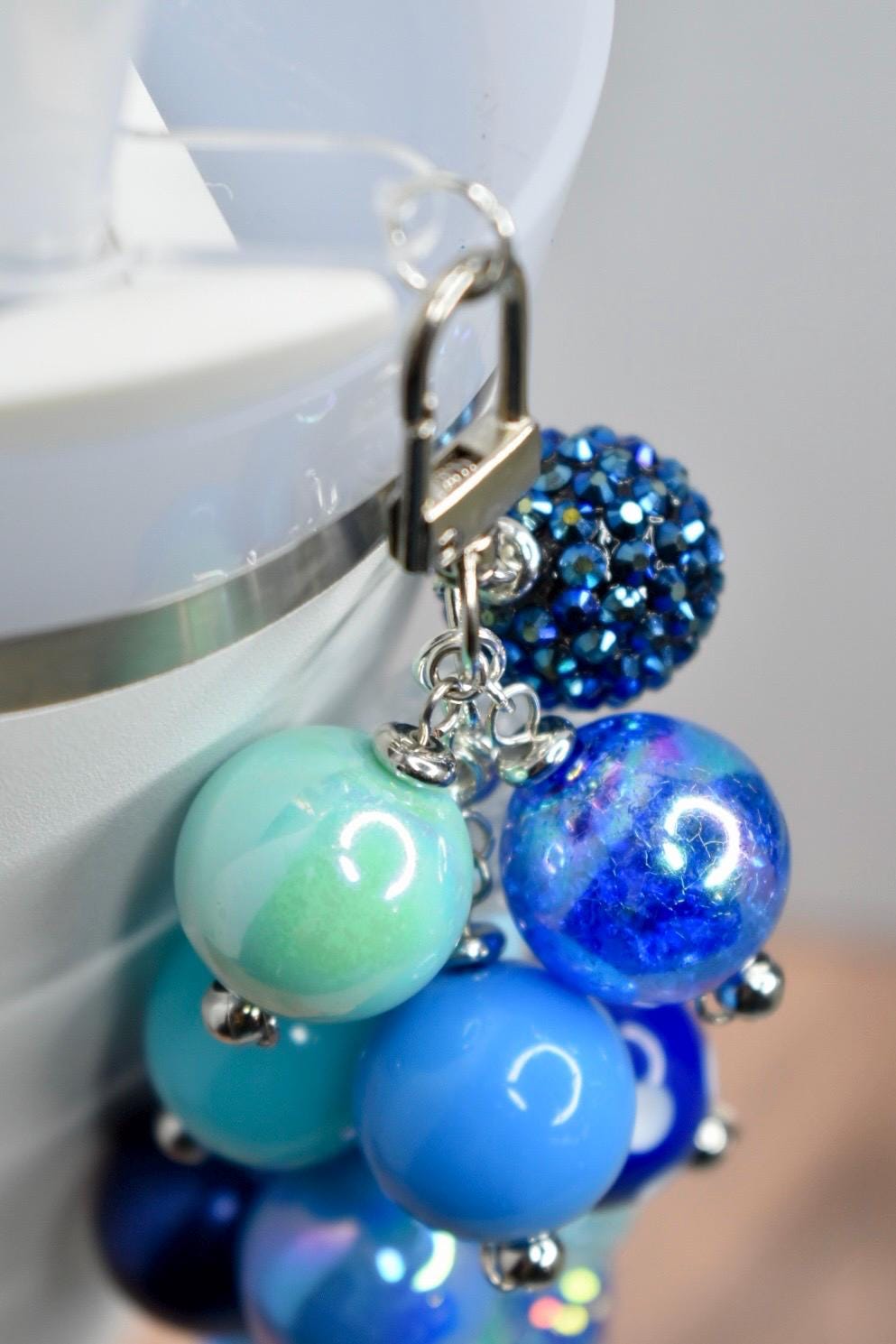 A collection of blue beaded charms with a silver clasp. The charms include various shades of blue, from light turquoise to deep navy, with a sparkling, jeweled accent bead. The beads are round and attached with silver findings.