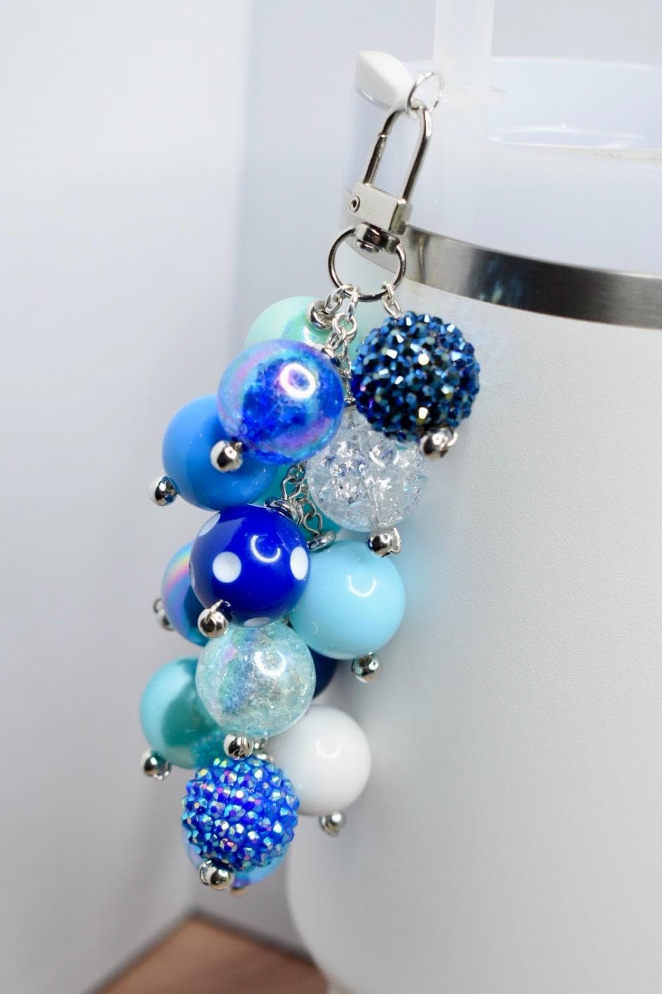 A beaded keychain with a variety of blue and white beads. The beads are in shades of light blue, dark blue, and white, with some having a glittery or textured appearance. The keychain is attached to a silver clasp.