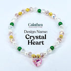 A beaded bracelet with a pink crystal heart pendant. The bracelet features clear, pink, green, and gold beads, with the text "Calathea Collective" and "Crystal Heart" visible.