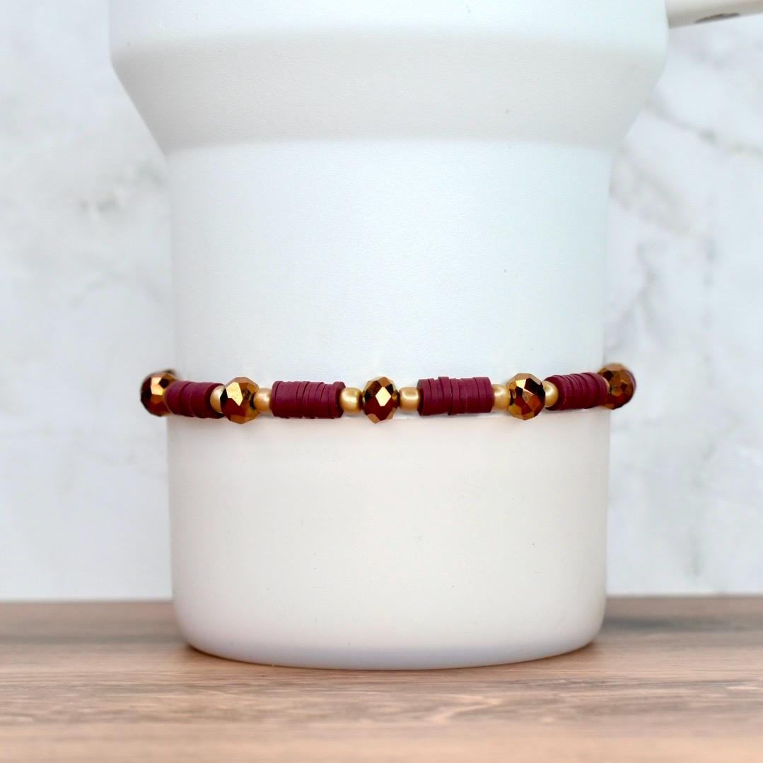 A burgundy and gold beaded bracelet. The bracelet features small, flat burgundy beads interspersed with gold-colored beads and faceted gold-colored beads. The bracelet is displayed against a white background.