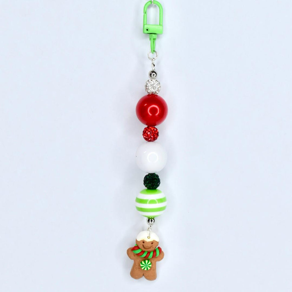 A Christmas-themed beaded keychain with a green clip. The keychain features red, white, and green beads, along with a gingerbread man charm. The gingerbread man has a white hat, a green and red scarf, and a green flower.