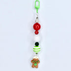 A Christmas-themed beaded keychain with a green clip. The keychain features red, white, and green beads, along with a gingerbread man charm. The gingerbread man has a white hat, a green and red scarf, and a green flower.