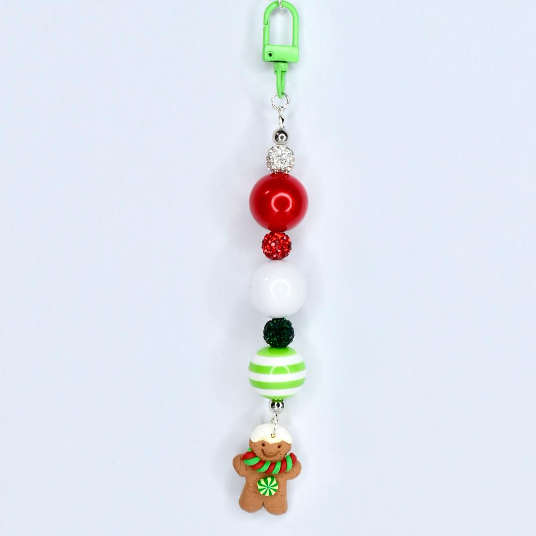 A Christmas-themed beaded keychain with a green clip. The keychain features red, white, and green beads, along with a gingerbread man charm. The gingerbread man has a white hat, a green and red scarf, and a green flower.