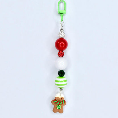 A Christmas-themed beaded keychain with a green clip. The keychain features red, white, and green beads, along with a gingerbread man charm. The gingerbread man has a white hat, a green and red scarf, and a green flower.