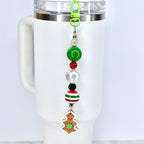A beaded charm with a green clasp, attached to a white tumbler. The charm features a series of beads in green, red, white, and black, culminating in a gingerbread man-shaped charm with a green flower.