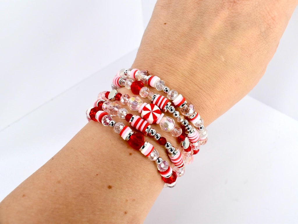 A stack of beaded bracelets in red, white, and clear. The bracelets feature a variety of beads, including small silver beads, red beads, and clear, faceted beads. Some beads have a candy cane stripe design.