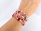 A stack of beaded bracelets in red, white, and clear. The bracelets feature a variety of beads, including small silver beads, red beads, and clear, faceted beads. Some beads have a candy cane stripe design.