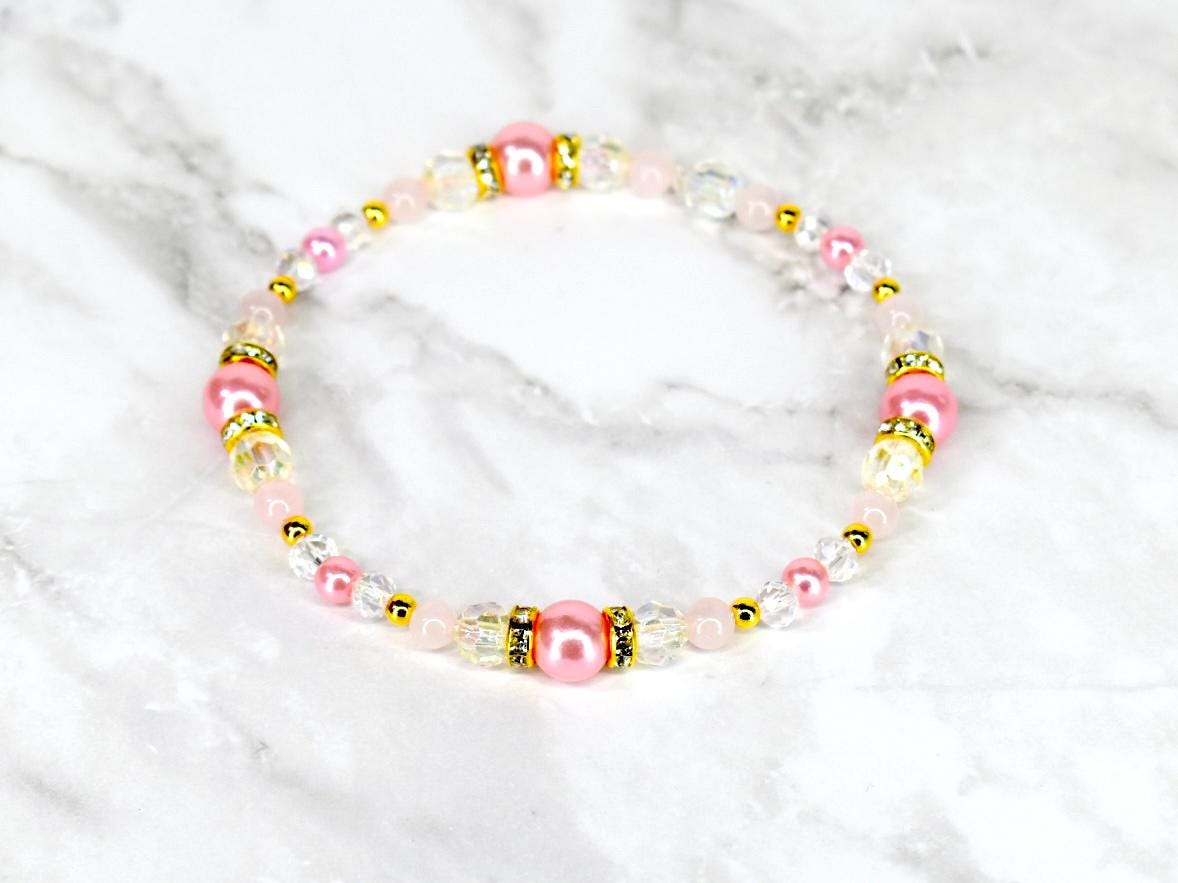 A delicate bracelet featuring pink and clear beads with gold accents. The bracelet has a mix of round and faceted beads, with larger pink pearl-like beads interspersed throughout. The gold accents add a touch of elegance.