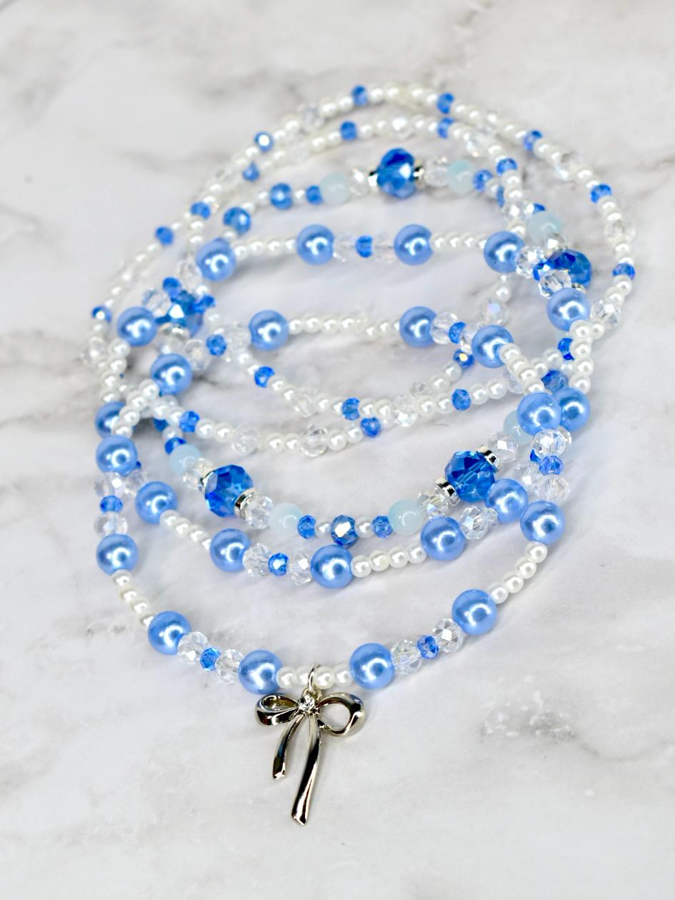 A set of five beaded bracelets featuring white and light blue beads, with a silver bow pendant. The bracelet stack has a mix of pearl and crystal beads. The light blue beads are a prominent feature, creating a delicate and elegant design.