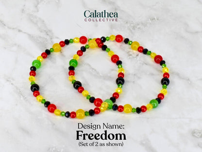 Two beaded bracelets with red, yellow, green, and black beads. The bracelets are labeled "Freedom" and are part of the Calathea Collective. The bracelets are shown on a white and gray marble surface.