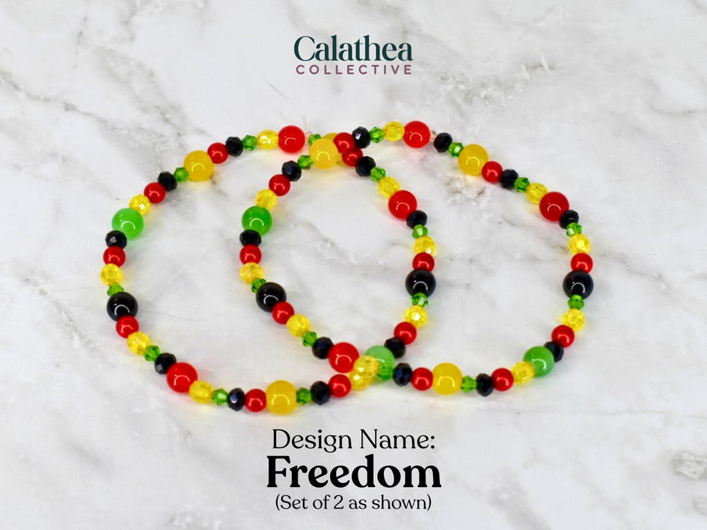 Two beaded bracelets with red, yellow, green, and black beads. The bracelets are labeled "Freedom" and are part of the Calathea Collective. The bracelets are shown on a white and gray marble surface.