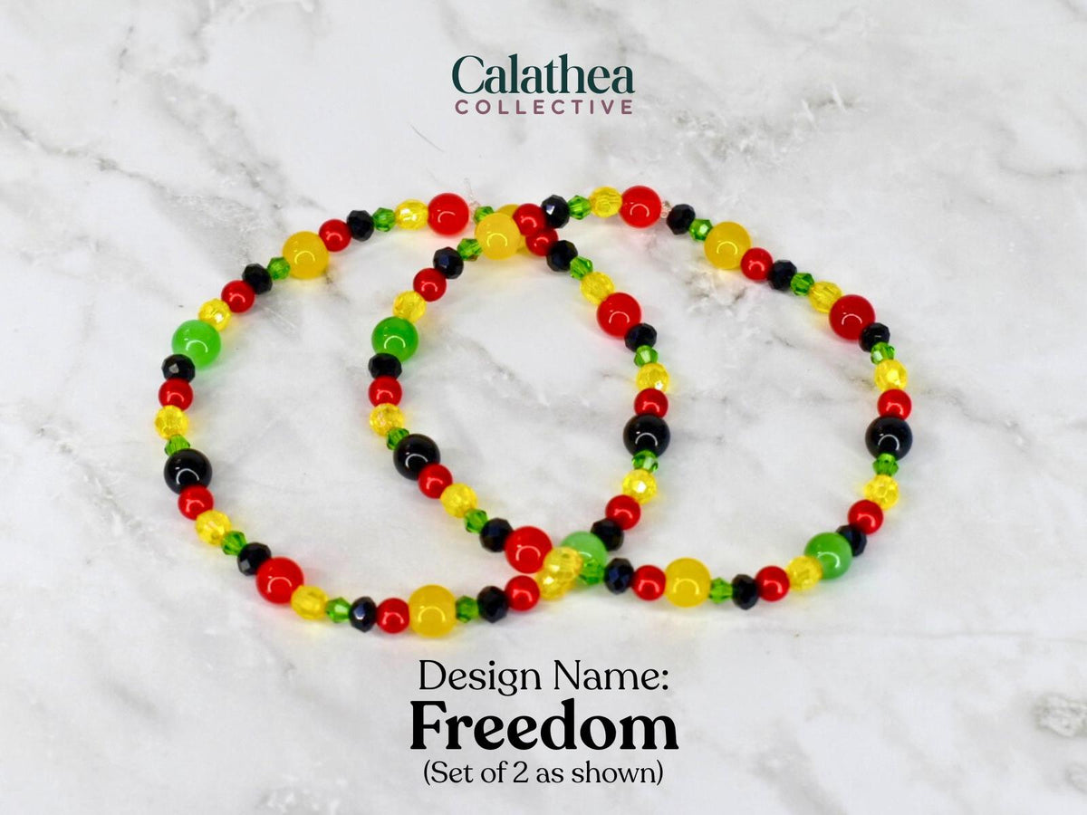 Two beaded bracelets with red, yellow, green, and black beads. The bracelets are labeled "Freedom" and are part of the Calathea Collective. The bracelets are shown on a white and gray marble surface.